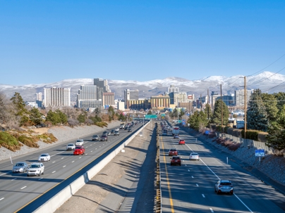 View of Interstate 80 in Reno, Nevada, with cars traveling in both directions and the city skyline and snow-capped mountains in the background. | Law Offices of Steven J. Klearman & Associates