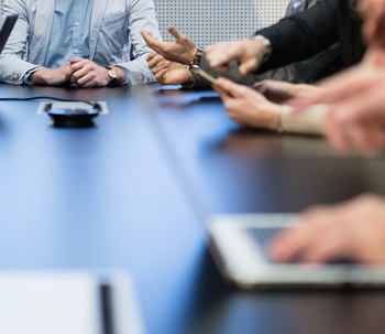 Image of people sitting around a table, with cell phones and tablets on the table top